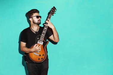 Elektro gitar ayakta mavi arka plan karşı oynarken bir yakışıklı tutkulu ifade serin genç esmer rock müzisyen erkek closeup