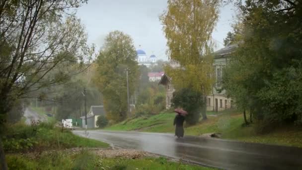 Perspektiv utsikt över prästen promenader längs vägen mittemot kyrkan i regnet. — Stockvideo