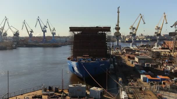 Al centro del porto si trova una nave commerciale blu bagnata dal mare. Molti magazzini e gru sul lato sinistro e destro della nave — Video Stock