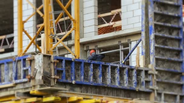 Le travail met les fenêtres par temps neigeux. Un travailleur dans un casque à la hauteur travaille sur un chantier de construction. — Video
