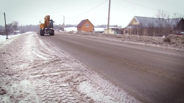 Straßenbauarbeiten. Bagger fahren auf einer schneebedeckten Straße vor dem Waldhintergrund. Wintertag — Stockvideo
