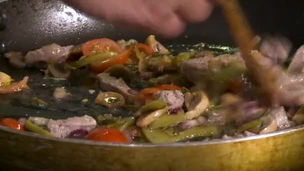 Vista da vicino di mani maschili che mescolano champignon per friggere, cipolle e carne in frypen oleoso. Preparazione della cena. — Video Stock