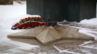 Kırmızı çiçeklerin arka planındaki sonsuz alevin anıtına yakından bak..