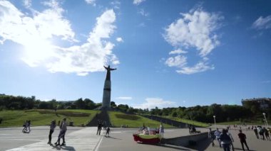 Ortasında aziz anıtı olan kalabalık bir şehir meydanı manzarası..