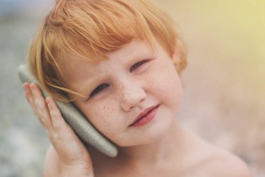 Kızıl saçlı kız kırmızı can simidi yakınındaki gemi duruyor, arka planda mavi deniz gibi.