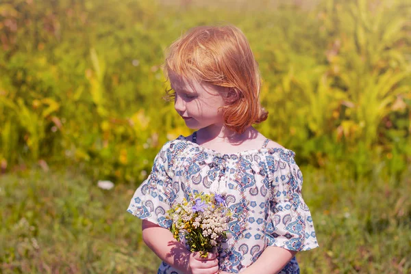 Carino allegra rossa ragazza che gioca sul prato, campo. Bella bambina nel prato vicino girasoli e sorridente. Luce solare morbida . — Foto Stock
