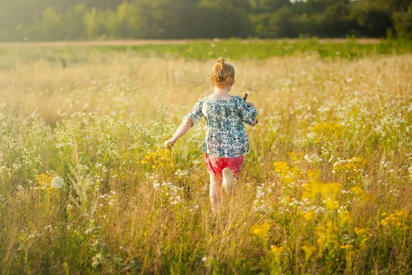 Giovane ragazza felice con un fiore in mano corre attraverso il campo . — Foto Stock