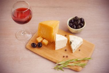 Bir kadeh kırmızı şarap, farklı peynir çeşitleri, zeytin, biberiye.