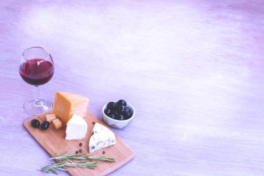 Bir kadeh kırmızı şarap, farklı peynir çeşitleri, zeytin, biberiye.