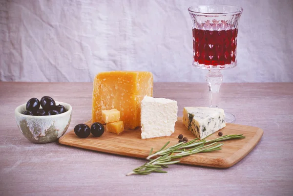 Ett glas rött vin, olika typer av ost, oliver, en kvist rosmarin. — Stockfoto