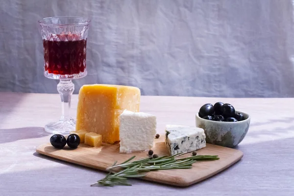Ett glas rött vin, olika typer av ost, oliver, en kvist rosmarin. — Stockfoto