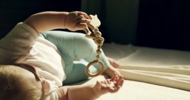 Yatakta ahşap oyuncak ile oynayan sevimli meraklı bebek yakın çekim. Küçük bebek karanlık odada gece ahşap oyuncaklar ile oynuyor