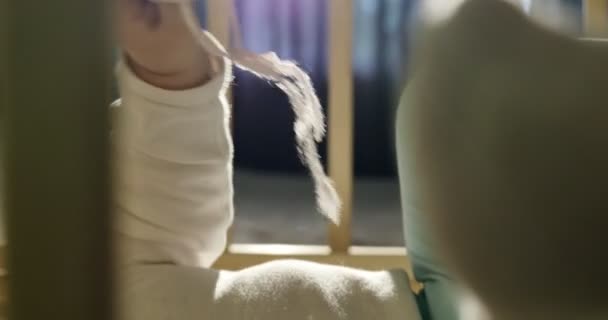 Närbild av bedårande nyfiken bebis leker med trä leksak i sängen. Lilla barnet leker med träleksaker på natten i mörkt rum — Stockvideo