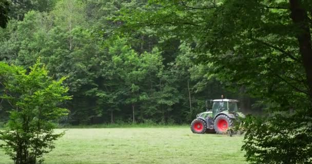 Traktor arbeitet auf dem Feld vor dem Hintergrund des grünen Waldes — Stockvideo