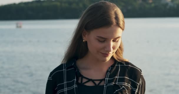 Nahaufnahme Porträt einer jungen attraktiven Frau, die bei Sonnenuntergang in Strandnähe lächelt und in die Kamera blickt — Stockvideo