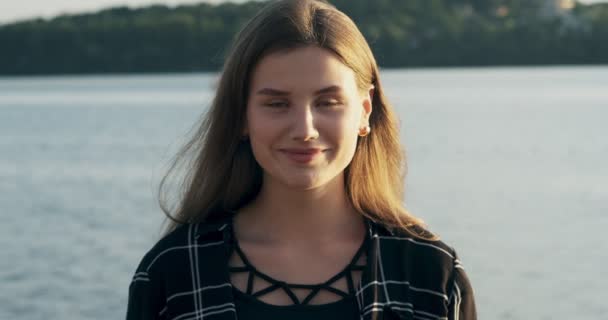Крупним планом портрет молодої привабливої жінки, посміхаючись і дивлячись на камеру біля пляжу на заході сонця впевнена краса — стокове відео