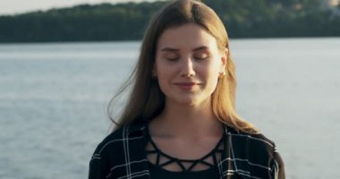 Genç çekici kadın gülümseyen ve gün batımında emin güzellik plaj yakınında kameraya bakarak yakın portre