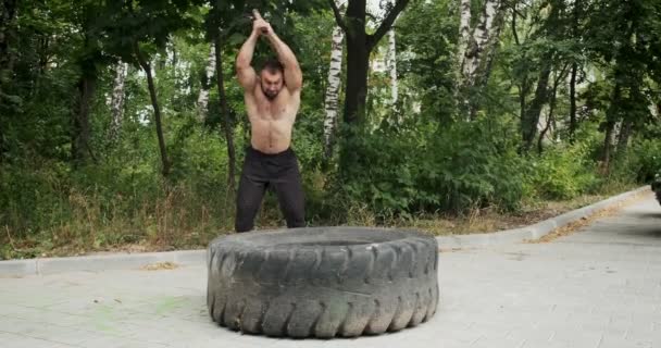 Muskel idrottare starke man träffar en hammare på ett stort hjul. Slow motion — Stockvideo