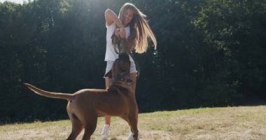 Mutlu genç bayan çimenlikte köpekle oynaşıyor. Evcil hayvanla aşk ve arkadaşlık