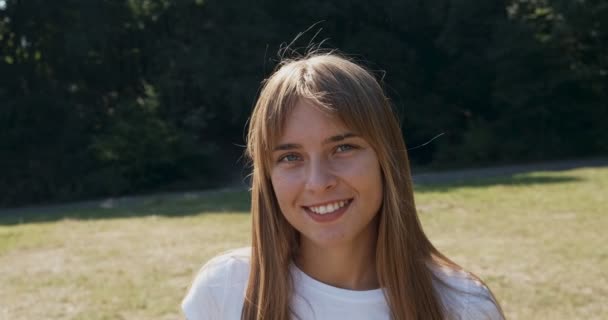 Posuvný portrét mladé atraktivní feny, která se usmívá a dívá se do kamery na zeleném trávníku. Veselá mladá dívka. Zavřít — Stock video