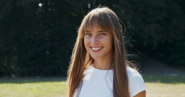 Portrét mladé atraktivní feny, která se usmívá a dívá se do kamery na zeleném trávníku. Veselá mladá dívka. Zavřít — Stock video