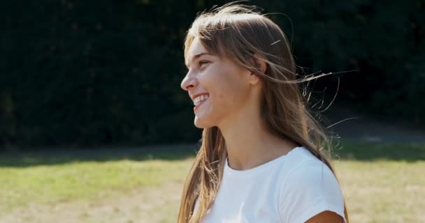 Portret van jonge aantrekkelijke vrouw die glimlacht en naar de camera kijkt op groen gazon. Vrolijk jong meisje. Sluiten. — Stockvideo