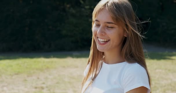 Portret van jonge aantrekkelijke vrouw die glimlacht en naar de camera kijkt op groen gazon. Vrolijk jong meisje. Sluiten. — Stockvideo