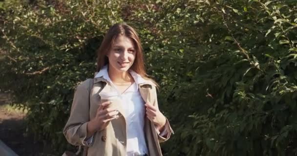 Jovem mulher de negócios atraente anda ao redor da área urbana verde histórica, com tirar xícara e beber café quente, olhando para a luz solar e pensando sobre o futuro, vestido em terno de negócios perto da parede do mato — Vídeo de Stock