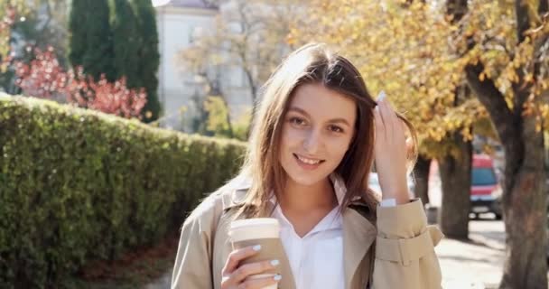 Jonge aantrekkelijke zakenvrouw loopt rond historische groene stedelijke gebied, met take away kopje en drink warme koffie, kijken naar zonlicht en denken aan de toekomst, gekleed in business suit in de buurt van bush muur — Stockvideo