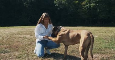 Mutlu genç bayan çimenlerde köpekle oynayarak neşeyle oynuyor. Evcil hayvanla aşk ve arkadaşlık