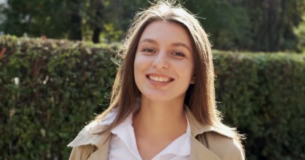 Ritratto di giovane femmina attraente che sorride e guarda la macchina fotografica sul verde storico urbano. Una bella donna allegramente. Da vicino. — Video Stock