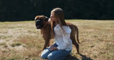 Mutlu genç bayan çimenlerde köpekle oynayarak neşeyle oynuyor. Evcil hayvanla aşk ve arkadaşlık