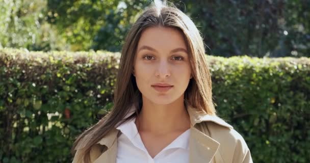 Retrato de una joven atractiva hembra que sonríe y mira a la cámara en el verde histórico urbano. Una mujer muy bonita y alegre. De cerca. — Vídeos de Stock