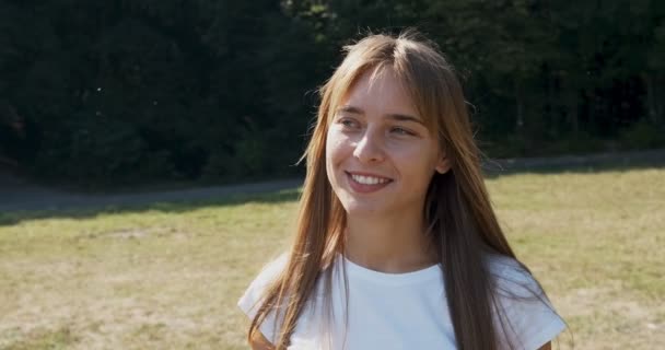 Joven atractiva caminata femenina y mirar a la cámara con sonrisa en el césped verde. Jovencita alegre — Vídeos de Stock