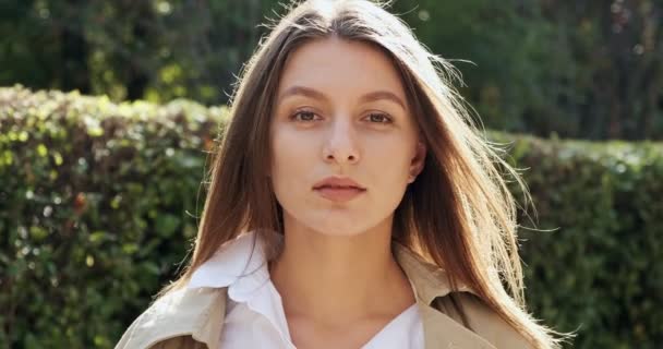 Retrato de una joven atractiva hembra que sonríe y mira a la cámara en el verde histórico urbano. Una mujer muy bonita y alegre. De cerca. — Vídeos de Stock