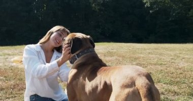 Mutlu genç bayan çimenlerde köpekle oynayarak neşeyle oynuyor. Evcil hayvanla aşk ve arkadaşlık