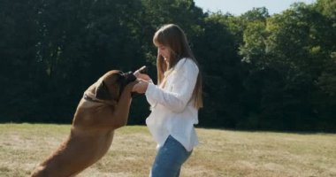 Mutlu genç bayan çimenlerde köpekle oynayıp koşuyor. Evcil hayvanla aşk ve arkadaşlık