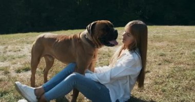 Mutlu genç bayan çimenlerde köpekle oynayarak neşeyle oynuyor. Evcil hayvanla aşk ve arkadaşlık