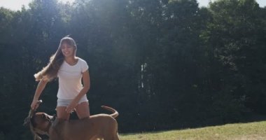 Mutlu genç bayan çimenlikte köpekle oynaşıyor. Evcil hayvanla aşk ve arkadaşlık