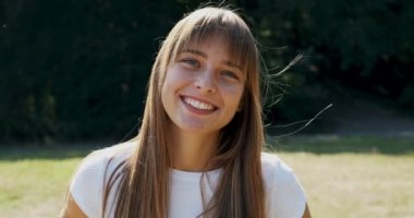 Yeşil çimenlikteki kameraya bakıp gülümseyen çekici bir kadının portresi. Neşeli genç kız. Kapat.