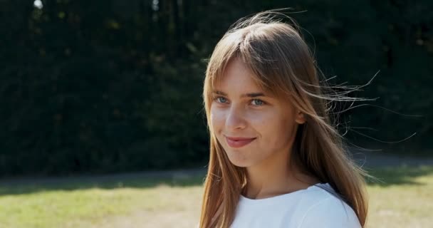 Ritratto di giovane femmina attraente che sorride e guarda la macchina fotografica sul prato verde. Ragazza giovane e allegra. Da vicino. — Video Stock