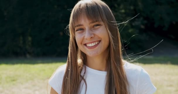 Retrato de una joven atractiva hembra que sonríe y mira a la cámara en el césped verde. Jovencita alegre. De cerca. — Vídeos de Stock