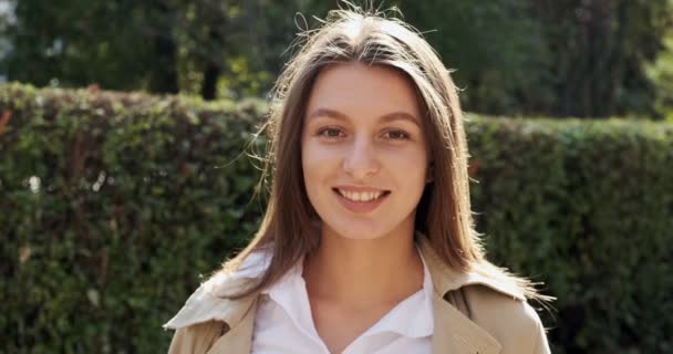 Retrato de jovem mulher atraente que sorrindo e olhando para a câmera na área urbana histórica verde. Uma mulher bonita e alegre. Fechar — Vídeo de Stock