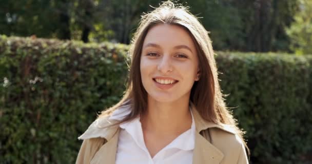 Retrato de una joven atractiva hembra que sonríe y mira a la cámara en el verde histórico urbano. Una mujer muy bonita y alegre. De cerca. — Vídeos de Stock