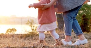 Genç bir anne temiz havada kızıyla el ele yürür. Mutlu bir aile gün batımında yeşil çimlerde yürüyor.