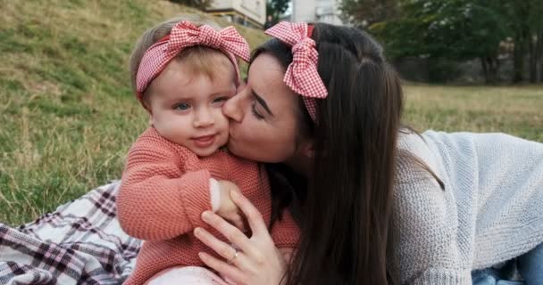 Mãe e uma filha pequena, passam o tempo juntos em um parque da cidade em um piquenique. Jovem mulher e menina estão jogando em uma planície na grama verde, ao pôr do sol — Vídeo de Stock