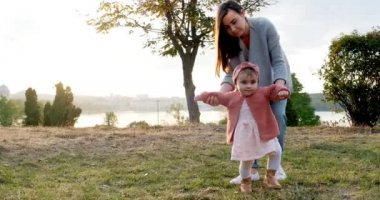 Genç bir anne temiz havada kızıyla el ele yürür. Mutlu bir aile gün batımında yeşil çimlerde yürüyor.