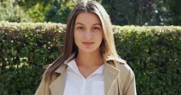 Retrato de una joven atractiva hembra que sonríe y mira a la cámara en el verde histórico urbano. Una mujer muy bonita y alegre. De cerca. — Vídeos de Stock