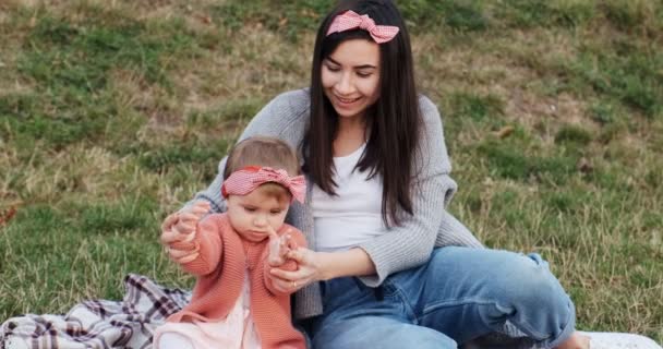 Moeder en een kleine dochter, brengt tijd samen door in een stadspark op een picknick. Jonge vrouw en klein meisje spelen op een ruit in groen gras, bij zonsondergang — Stockvideo