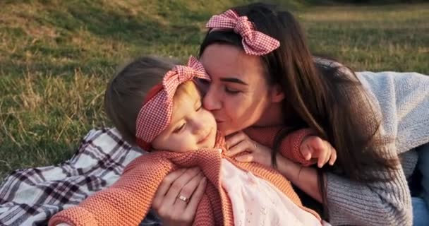 Moeder en een kleine dochter, brengt tijd samen door in een stadspark op een picknick. Jonge vrouw en klein meisje spelen op een ruit in groen gras, bij zonsondergang — Stockvideo